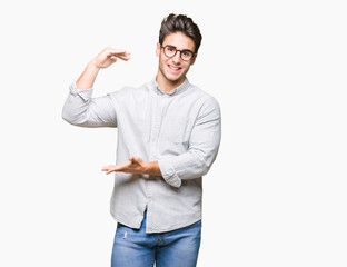Young handsome man wearing glasses over isolated background gesturing with hands showing big and large size sign, measure symbol. Smiling looking at the camera. Measuring concept.