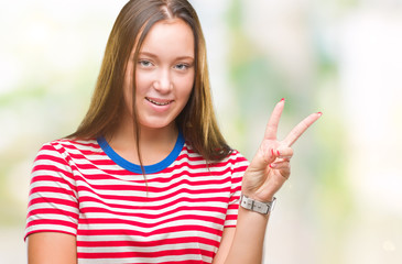 Young caucasian beautiful woman over isolated background smiling with happy face winking at the camera doing victory sign. Number two.