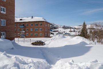 Car stands among the high snowdrifts in the courtyard of a residential building.