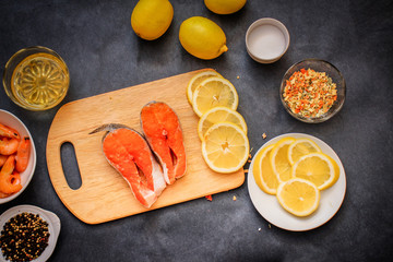 Wooden board in the middle of the frame with the salmon laid out in a plate raw shrimp pepper lemon...