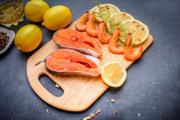 On a gray tabletop runs a wooden board on which salmon raw shrimp lemon slices pepper oil seasoning.