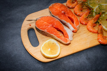 Closeup of chopped salmon with lemon slice on wooden board on gray crafty table top.