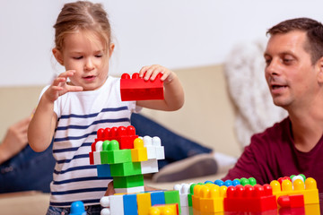 Smiling man and little daughter playing with cubes together at home.