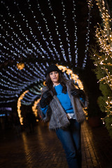 Pretty dark haired girl wearing a fur coat, blue jeans, blue top and a black hat, smiling, posing...