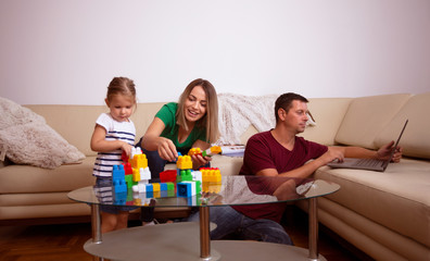 Smiling mother playing with her daughter and father working.