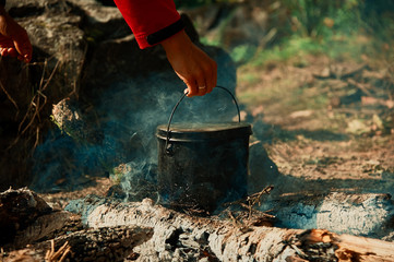 A woman prepares food on a campfire for her husband. Hands close up.