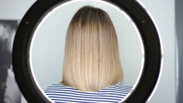 Master hairdresser makes a photo of the just trimmed girl with LED ring. Ring LED flash for portrait of a young beautiful blonde woman