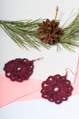Knitted earrings on the background of felt fabric. Near pine branch with a cone.