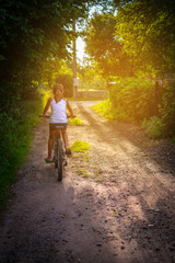 Fototapeta premium Childhood bliss: girl happily riding a bicycle on a rural dirt road