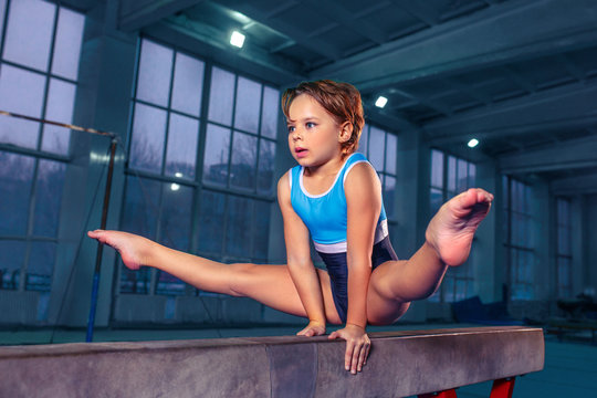 The beautiful little girl is engaged in sports gymnastics on a log at gym. The performance, sport, acrobat, acrobatic, exercise, training concept