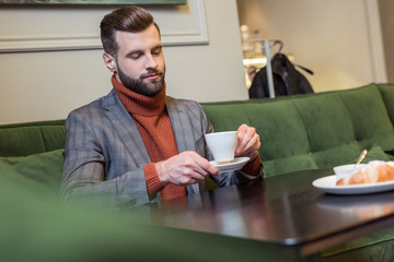 selective focus of handsome man in formal wear sitting at table and drinking coffee in restaurant