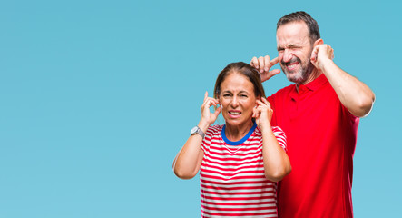Middle age hispanic couple in love over isolated background covering ears with fingers with annoyed expression for the noise of loud music. Deaf concept.