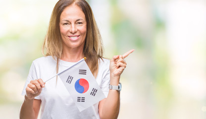 Middle age hispanic woman holding flag of South Korea over isolated background very happy pointing with hand and finger to the side
