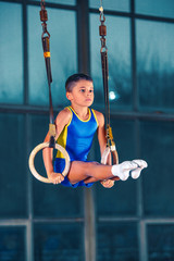 Full length shot of male athlete performing pull-ups on gymnastic rings. Fitness boy with strong body exercising at gym. The performance, sport, acrobat, acrobatic, exercise, training concept