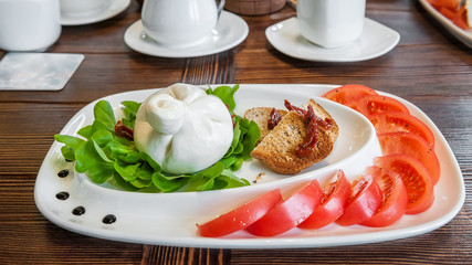 Burato cheese and lettuce for the correction of the weight of the leaves of Lollo Rosso lettuce and tomatoes. Restaurant food. The concept of healthy eating.