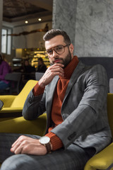 pensive man in formal wear and glasses sitting and looking at camera in restaurant