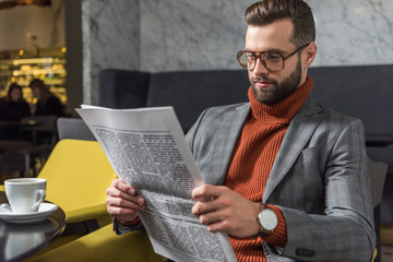 focused stylish man in formal wear and glasses sitting and reading newspaper in restaurant