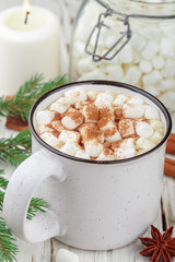 Hot cocoa (coffee or chocolate) with marshmallows and cinnamon in a white Cup. Candy, candles and fir branches on the table. Christmas. New year. Rustic style. Selective focus
