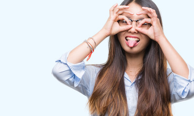 Young asian business woman wearing glasses over isolated background doing ok gesture like binoculars sticking tongue out, eyes looking through fingers. Crazy expression.