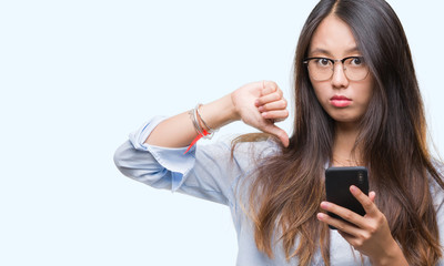 Young asian woman texting using smartphone over isolated background with angry face, negative sign showing dislike with thumbs down, rejection concept