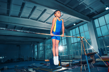 The little boy is engaged in sports gymnastics on a parallel bars at gym. The performance, sport, acrobat, acrobatic, exercise, training concept