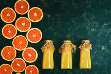 Orange juice in bottles and orange halves on a dark background. Top view, flat lay, copy space....