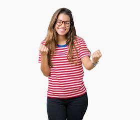 Obraz na płótnie Canvas Young beautiful brunette woman wearing glasses and stripes t-shirt over isolated background very happy and excited doing winner gesture with arms raised, smiling and screaming for success
