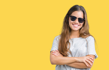 Young beautiful brunette woman wearing sunglasses over isolated background happy face smiling with crossed arms looking at the camera. Positive person.