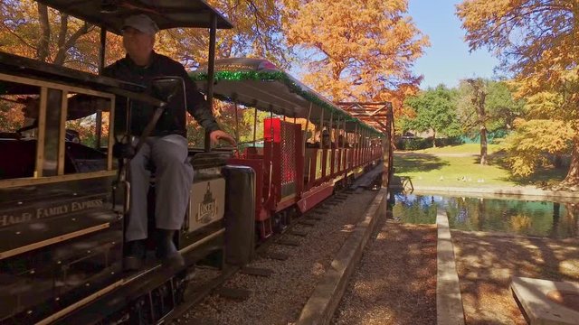 Mini size steam engine old cowboy style locomotive that people ride on through the park and over mini rail road bridge.
