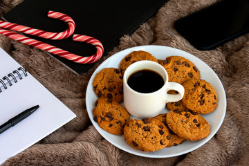 Cozy winter composition with homemade chocolate cookies, book, notebook on soft blanket. Holiday relaxation.