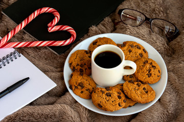 Cozy winter composition with homemade chocolate cookies, book, notebook on soft blanket. Holiday relaxation.