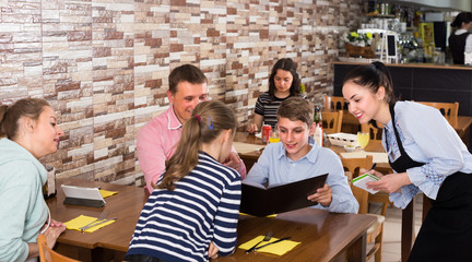 Happy parents with children are giving order to cheerful waitress