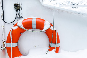 Lifebuoy ring on white boat in winter covered with snow. Safety equipment on the boat. Orange life...
