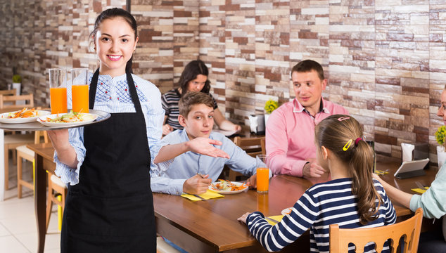 cheerful young waitress warmly welcoming guests to family cafe