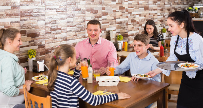 friendly brunette waitress serving family in family cafe