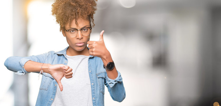 Beautiful young african american woman wearing glasses over isolated background Doing thumbs up and down, disagreement and agreement expression. Crazy conflict