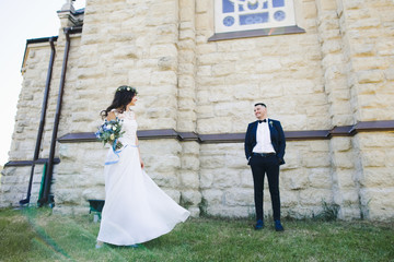 Stunning and happy wedding couple poses on the green lawn before an old church