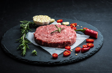 Raw ground beef meat burger steak cutlet with chili, rosemary and garlic on black slate plate for cooking