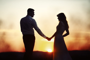 Silhouettes of bride and groom standing on the field before the red sunset