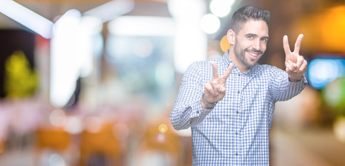 Young handsome man over isolated background smiling looking to the camera showing fingers doing victory sign. Number two.