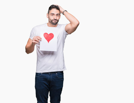 Handsome young man holding card with red heart over isolated background stressed with hand on head, shocked with shame and surprise face, angry and frustrated. Fear and upset for mistake.