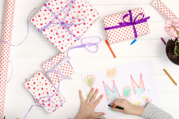 Obraz premium Little girl drawing happy mother's day greeting card with presents on the table. Mothers day background