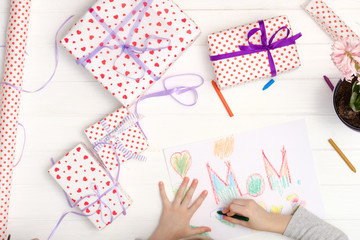 Little girl drawing happy mother's day greeting card with presents on the table. Mothers day background