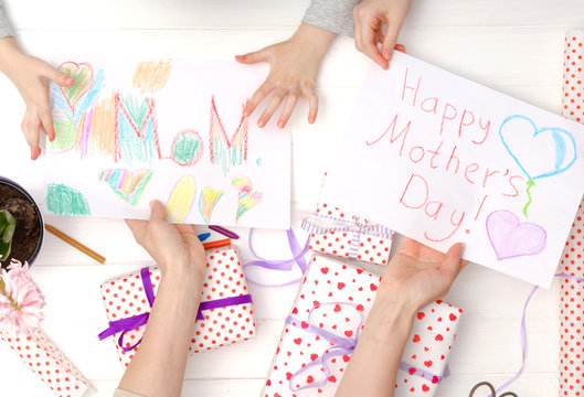Happy mother's day card made by little child. Girl's hands holding a handmade cards with giftboxes. I love you, mom