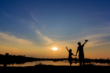 Fototapeta na wymiar silhouette of father and son stood holding hands arms lake on sunset.