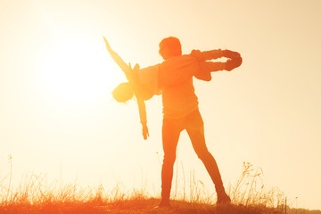 Happy mother raising her little daughter in the air. Mother and daughter playing airplane game at sunset. Mother and daughter silhouette