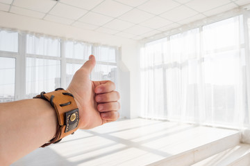 Male hand with brown leather bracelet showing thumbs up sign against white background. Man's hand...