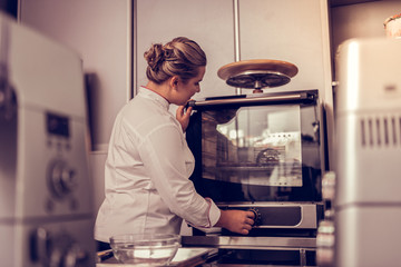 Professional skilled cook turning on the oven