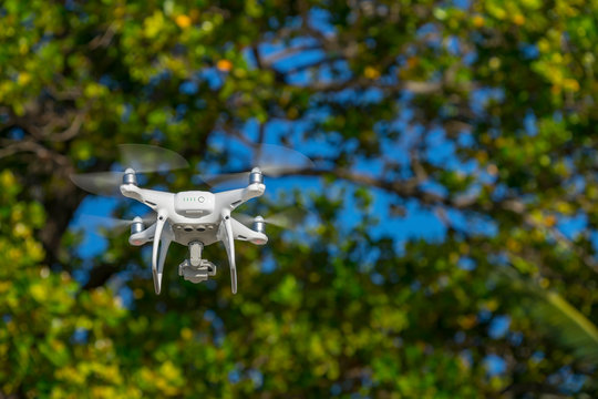 Drone in flight, green trees in the background, selective focus on the drone.