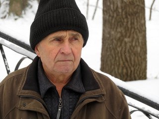 Portrait of old man in black knitted hat during a snowfall. Concept of cold weather, snow winter, homeless or poverty